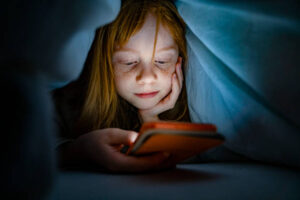 Girl using a mobile phone in the night. Kid skipping sleep hooked on the phone