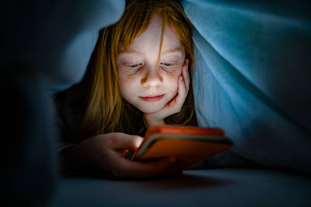 Girl using a mobile phone in the night. Kid skipping sleep hooked on the phone